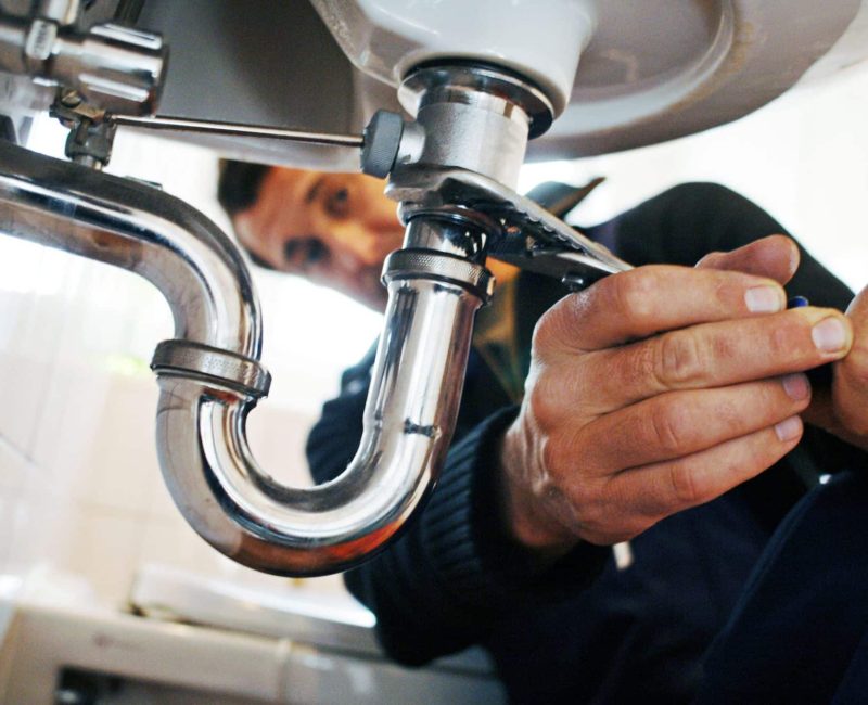 Close-up of plumber repairing sink. Male worker using tool while fixing appliance in bathroom. He is working on metallic equipment at home.